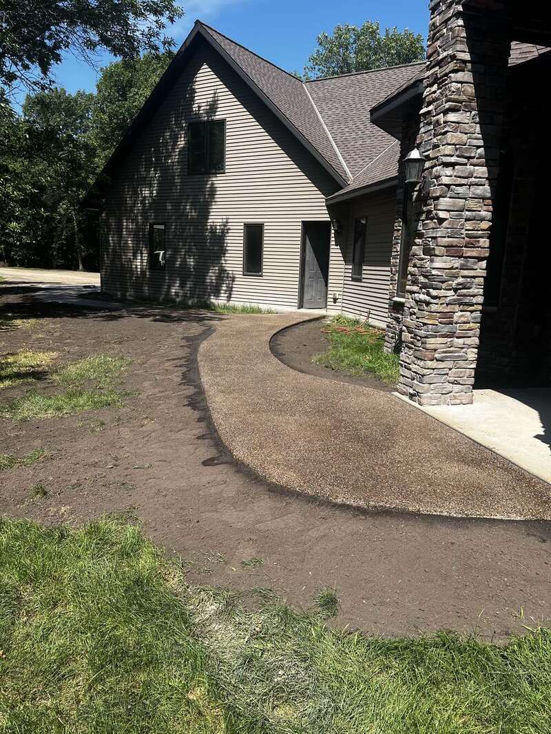 Curved exposed aggregate front entry walkway to a stone-columned entrance