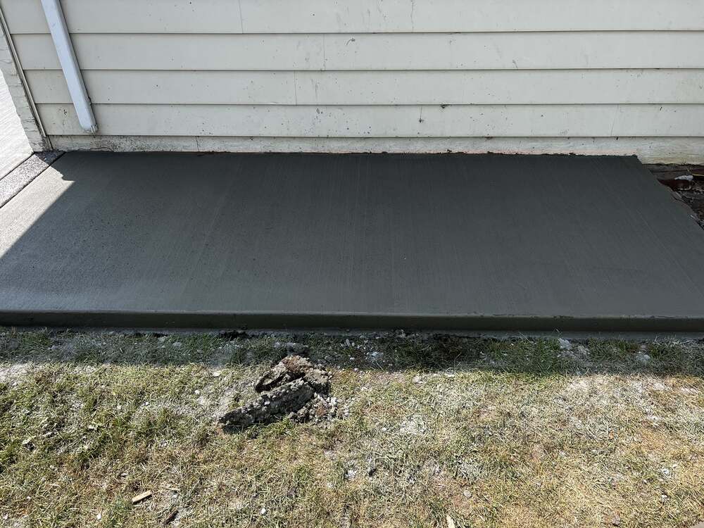 Freshly poured broom-finish concrete sidewalk section along a home